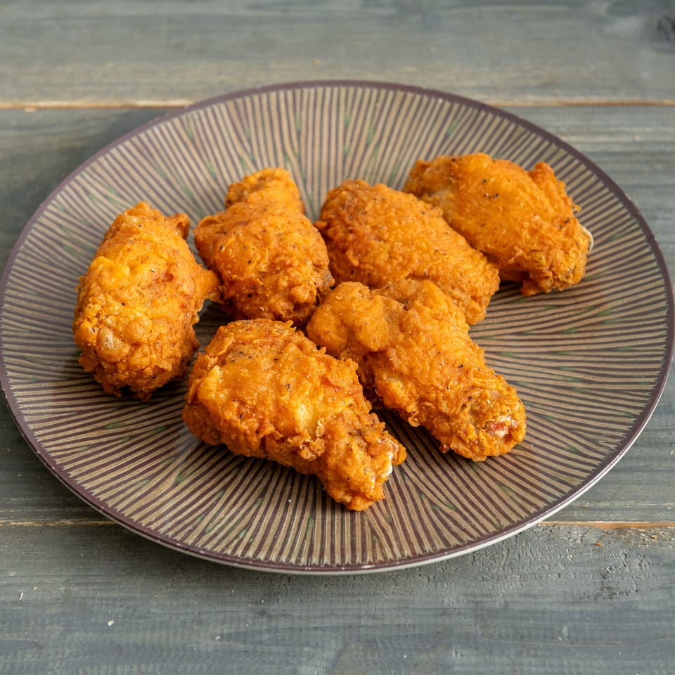 A plate of golden-brown fried chicken pieces sits on a patterned platter atop a rustic wooden table.