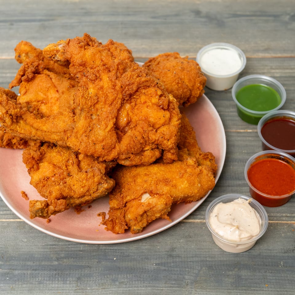 Plate piled with crispy fried chicken pieces alongside cups of white, green, red, and orange dipping sauces.