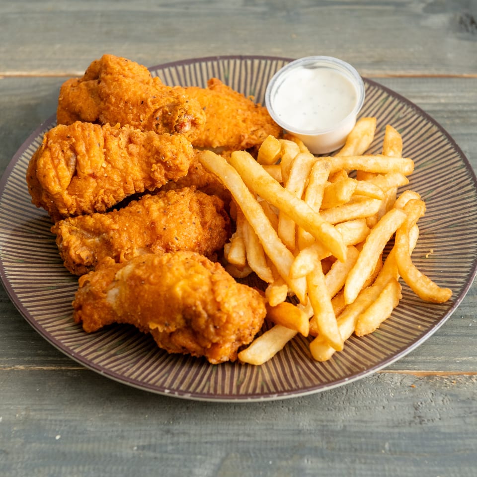 Crispy fried chicken pieces with golden French fries and creamy dipping sauce on a patterned plate.