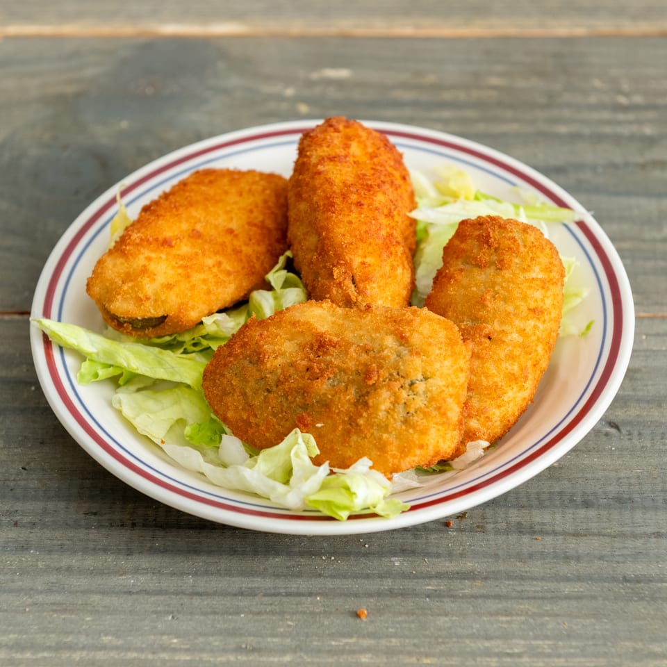 Plate of golden-brown breaded croquettes served over fresh lettuce on a rustic wooden table.
