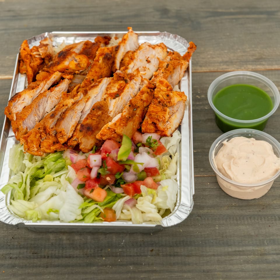 Tray of seasoned grilled chicken over lettuce and chopped salad, served with green herb and creamy sauces.